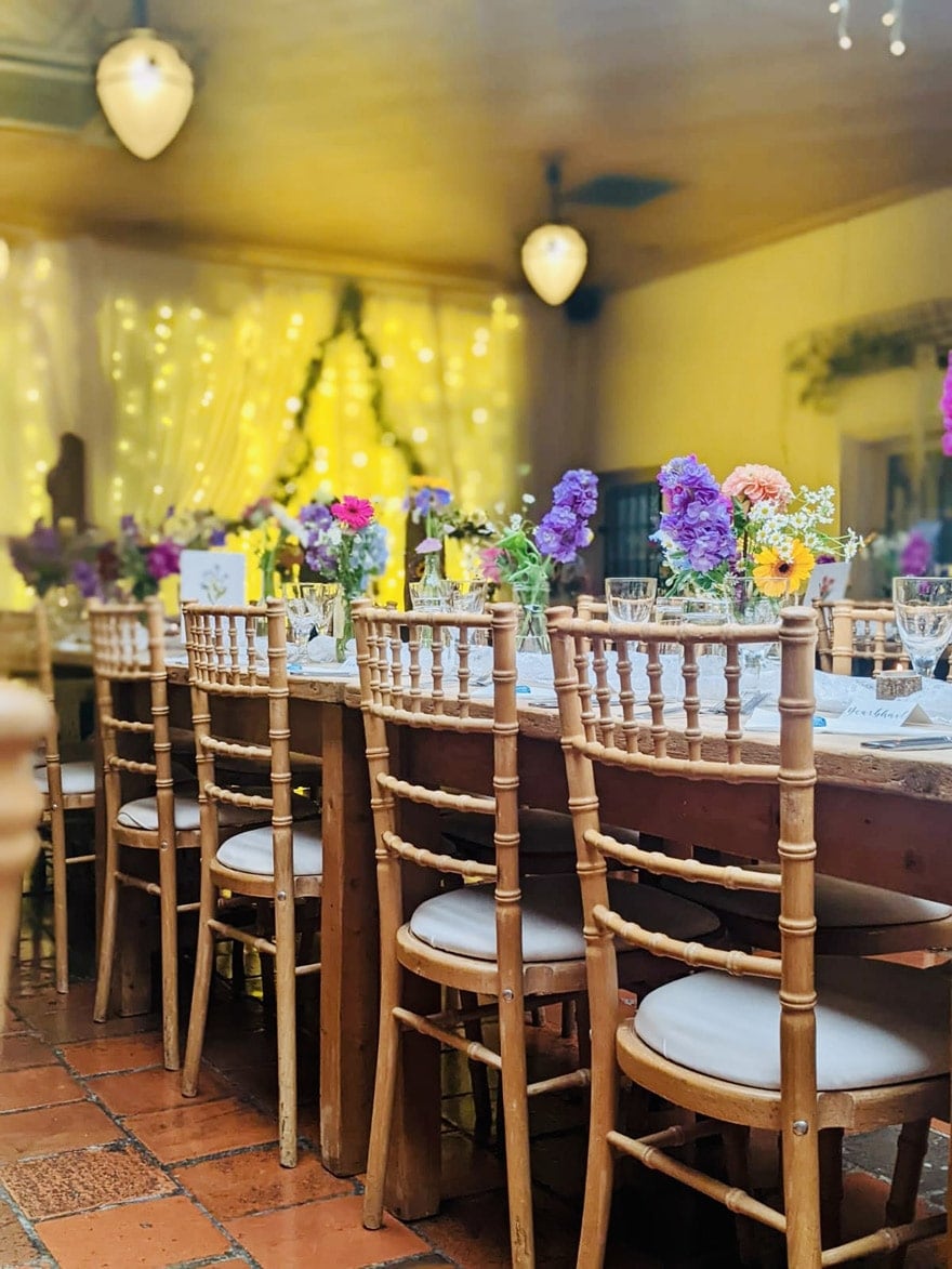 A long event table set with flowers, glasses and wooden chairs